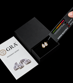 A pair of gold diamond stud earrings displayed in a black jewelry box, with a GIA diamond report card and a diamond selector probe visible on a black background.