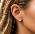 A close-up of a woman's ear wearing a small pear-cut clear gemstone stud earring in a silver-toned setting.